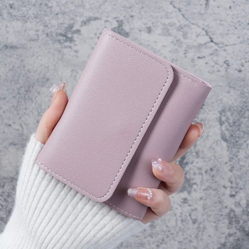 A hand holds a light mauve slim triple-fold PU leather wallet against a gray textured background.