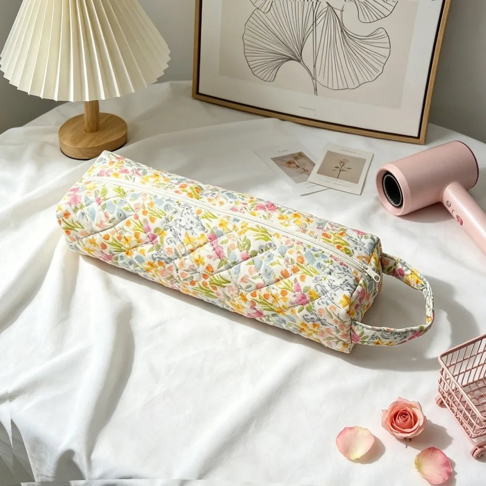 A quilted cotton hair dryer storage bag with a floral pattern rests on a white surface next to a lamp and framed art.