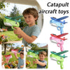A boy is holding a green foam catapult airplane toy outdoors, demonstrating its use.