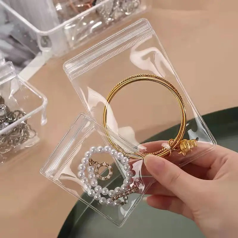 A hand holds a clear plastic jewelry pouch containing a gold ring and a pearl necklace.