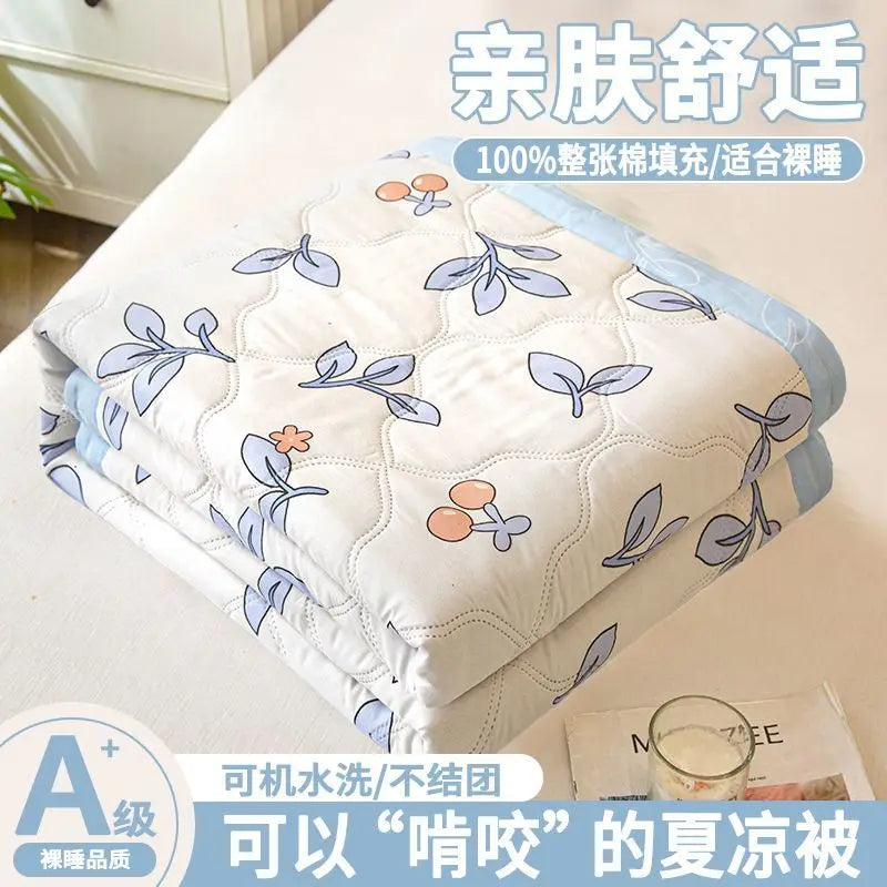 A stack of white quilted fabric featuring light blue leaf patterns, marketed as an ultra-light breathable summer quilt.