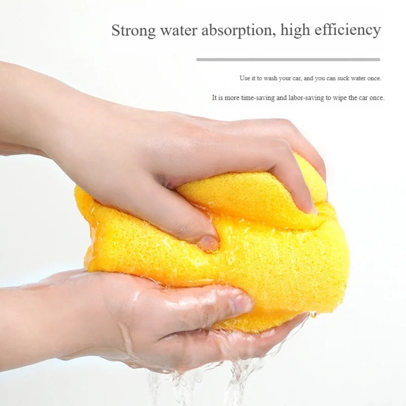 Hands are squeezing a bright yellow, high-density car wash sponge onto a surface.