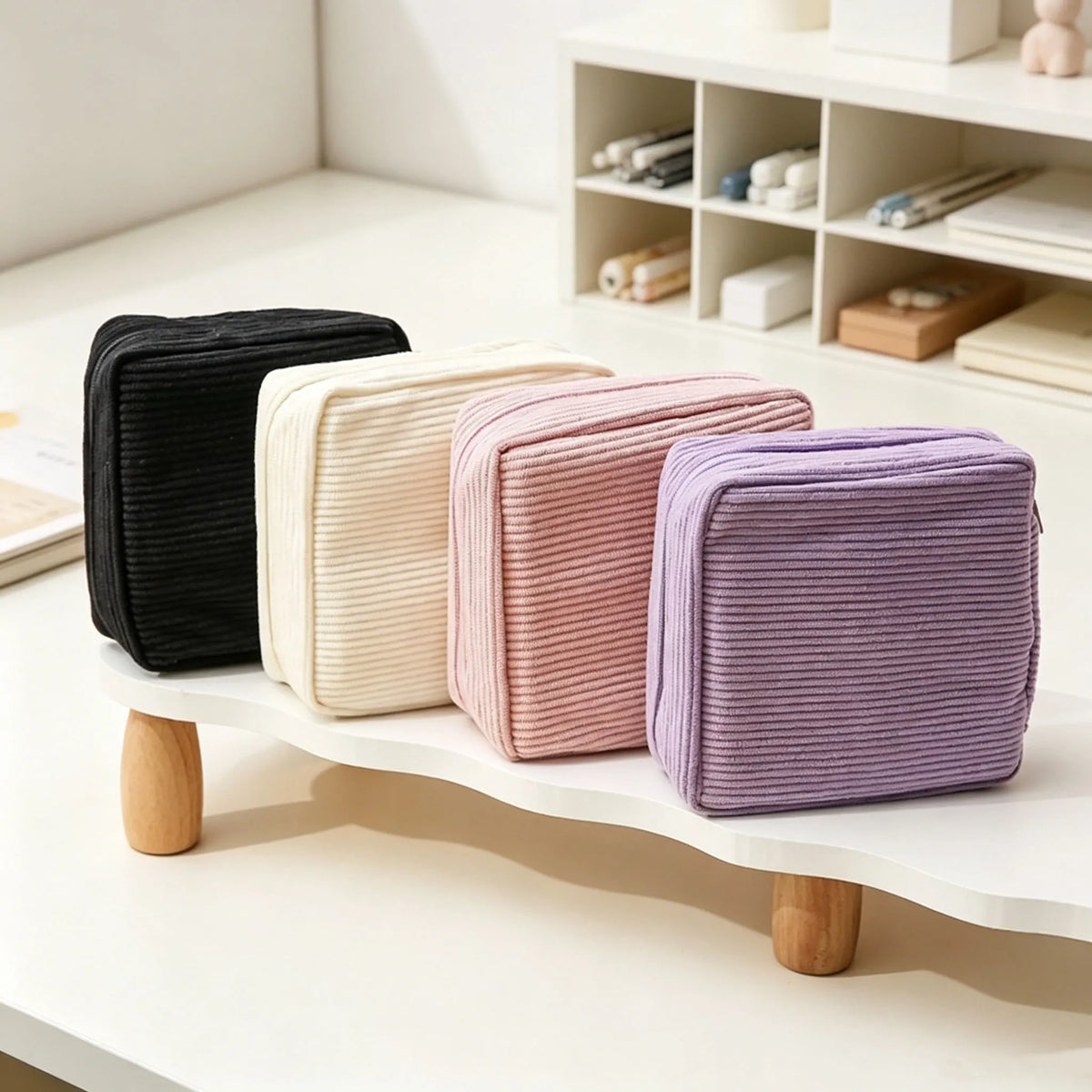 A row of stacked, striped fabric pouches in black, cream, pink, and purple are displayed on a white shelf.