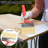 A hand is using a red paint brush with natural bristles to apply paint on a wooden table.