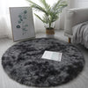 A round, dark gray shaggy area rug placed on a light floor next to a potted palm plant and framed artwork.