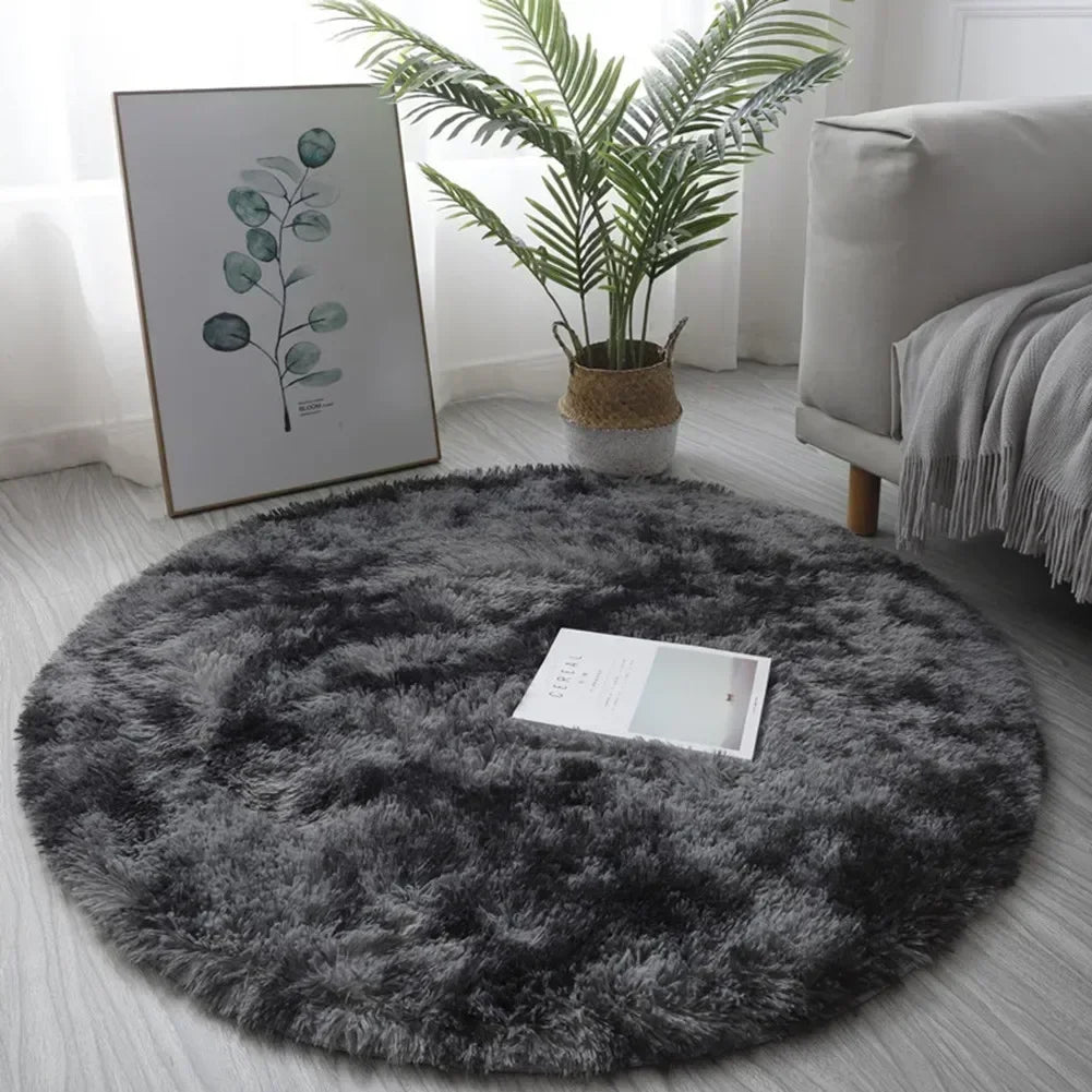 A round, dark gray shaggy area rug placed on a light floor next to a potted palm plant and framed artwork.