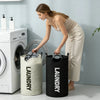 A woman is placing laundry into a large black fabric laundry basket next to a white washing machine.