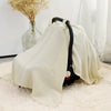 A beige breathable cotton muslin car seat and stroller cover draped over a light pink rug.