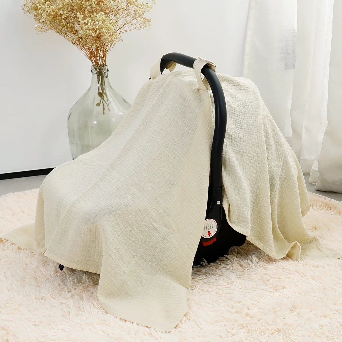 A beige breathable cotton muslin car seat and stroller cover draped over a light pink rug.