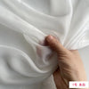 A hand is gently folding a piece of white, lightweight, sheer mulberry silk chiffon fabric.