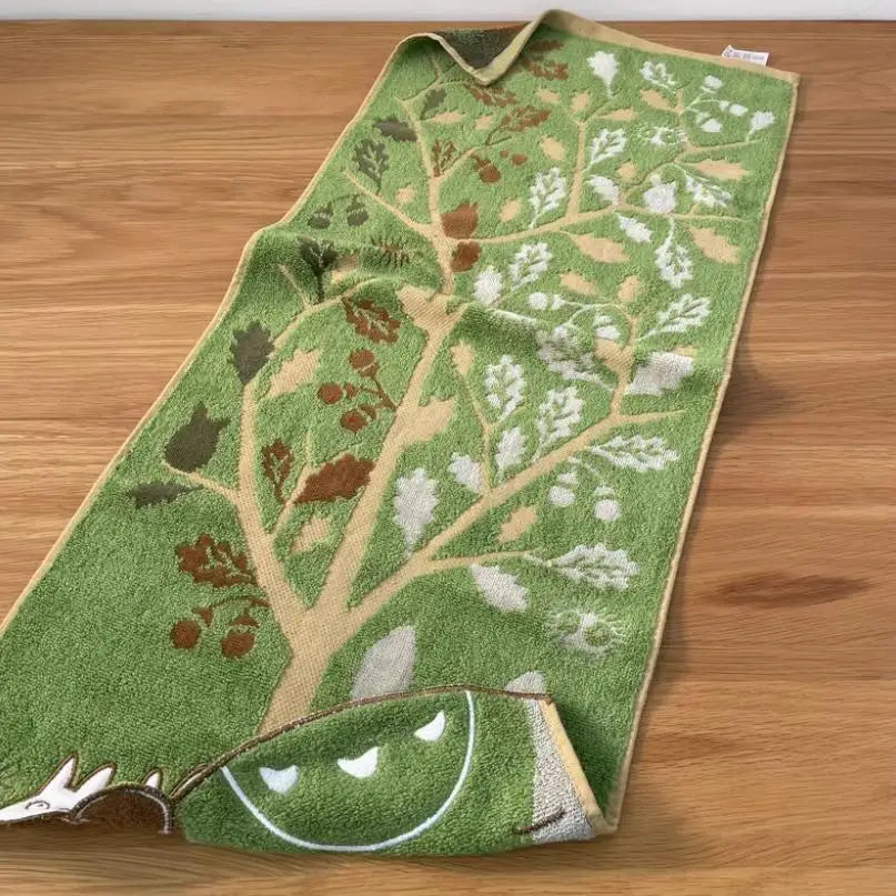 A green towel embroidered with a tree and cartoon animal face design