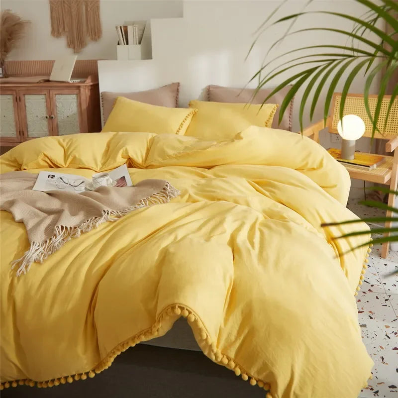 A bright yellow duvet cover set with a soft, textured fabric and pom-pom trim displayed on a bed.