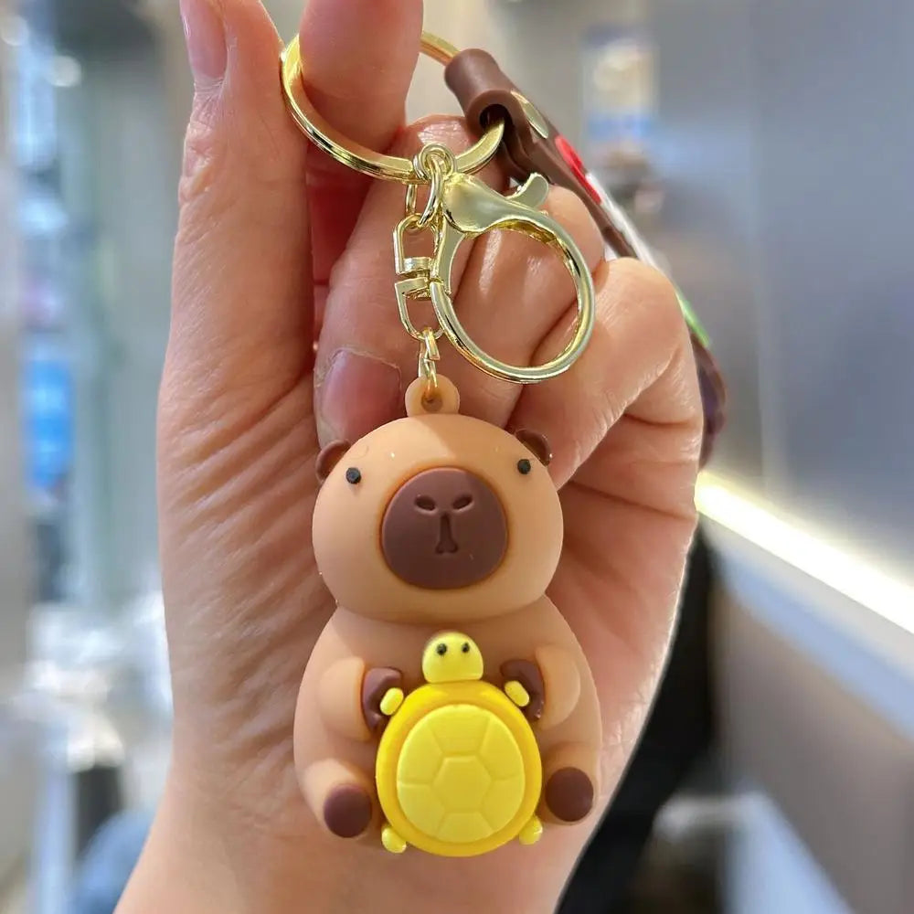 A hand holds an adorable capybara keychain charm featuring a small yellow turtle inside.