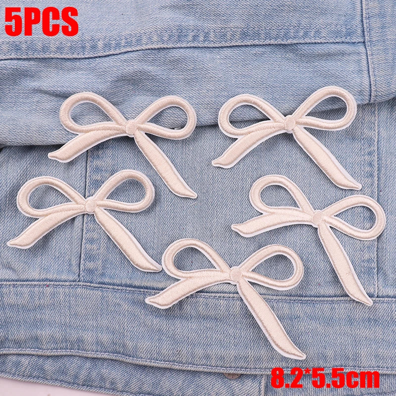 Five embroidered white cartoon bow iron-on patches displayed on a denim fabric.