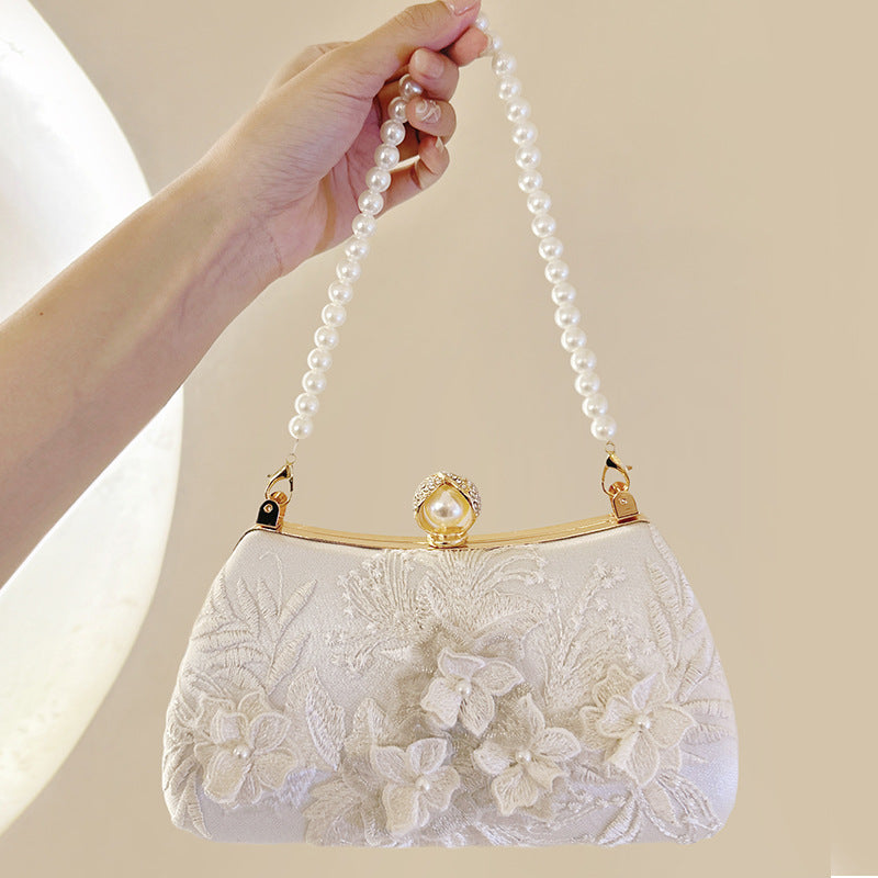 A pale pink pearl embroidered evening clutch with a gold chain strap being held by a hand.