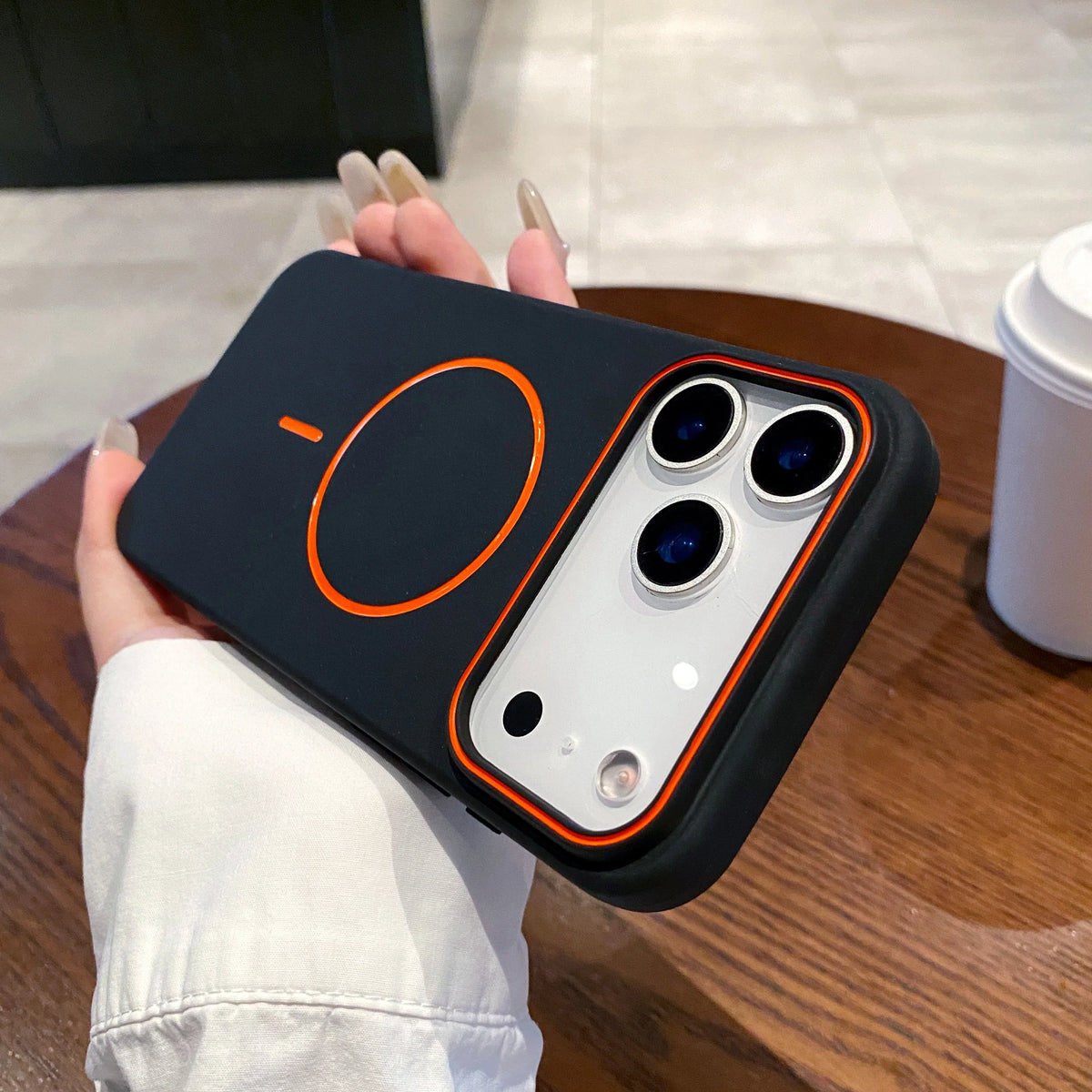 A hand holds a black magnetic phone case with MagSafe support on a wooden table.