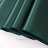 A close-up of an elegant dark emerald green satin table runner rolled up.