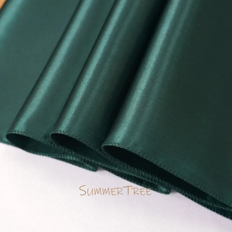 A close-up of an elegant dark emerald green satin table runner rolled up.