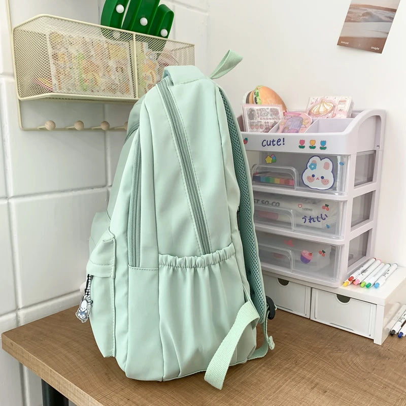 A light mint green waterproof nylon laptop backpack with ergonomic straps resting on a wooden surface.