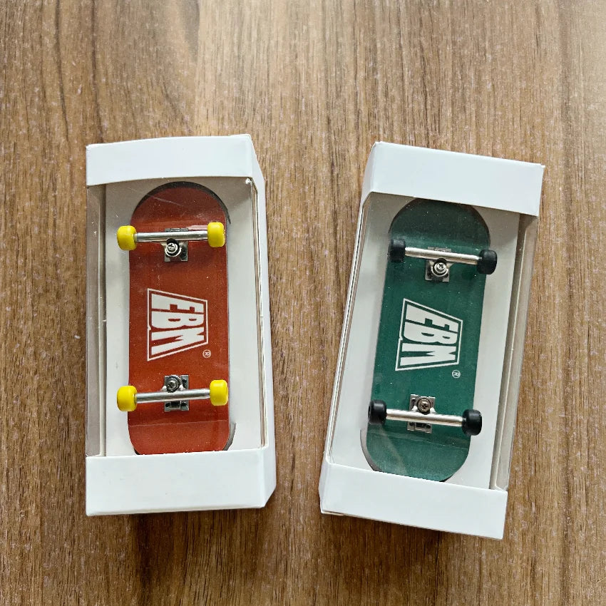 A wooden fingerboard skateboard with realistic trucks is displayed in a white box on a wooden surface.