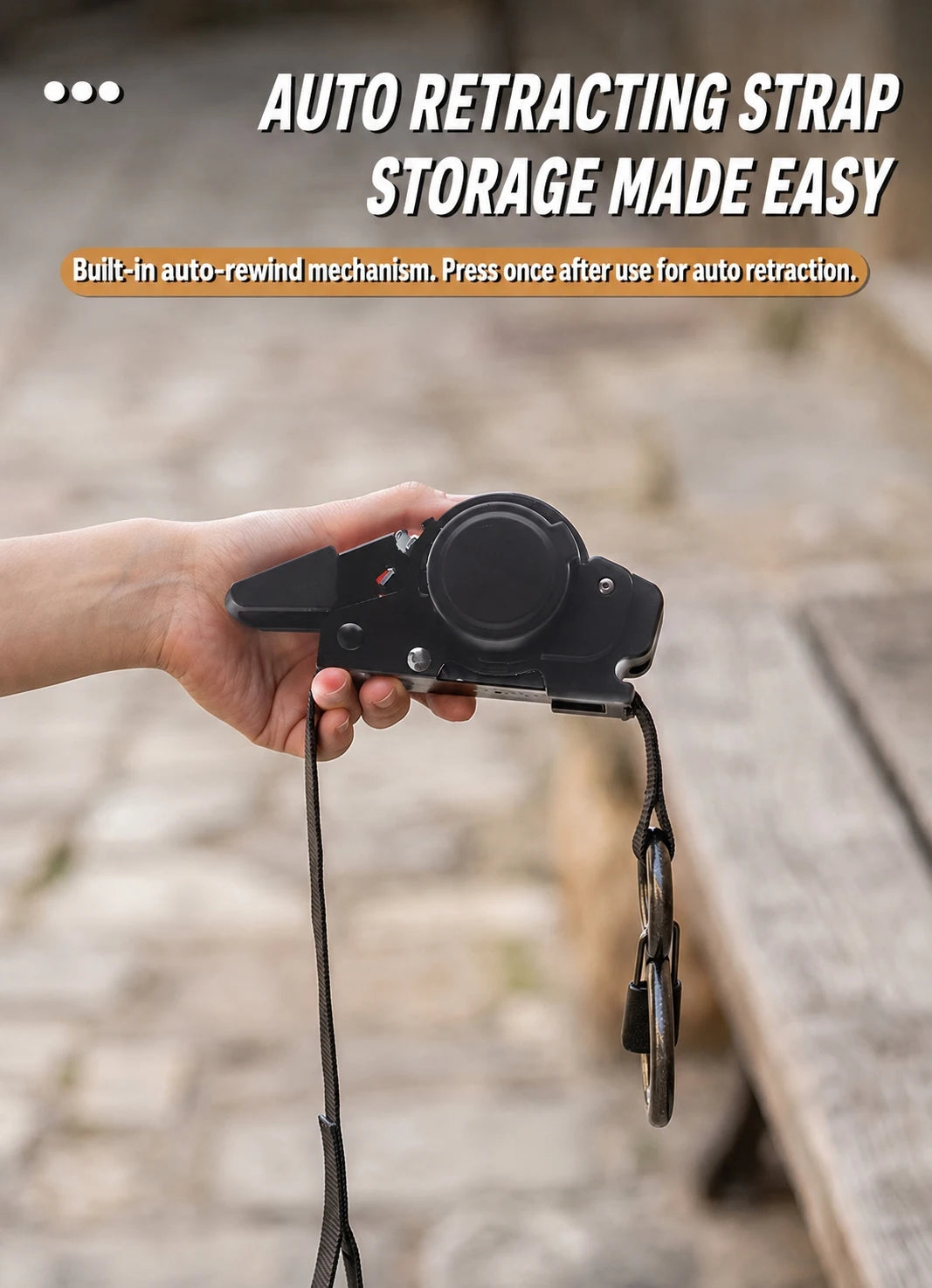 A hand holds an auto retracting strap storage device with a black strap attached.