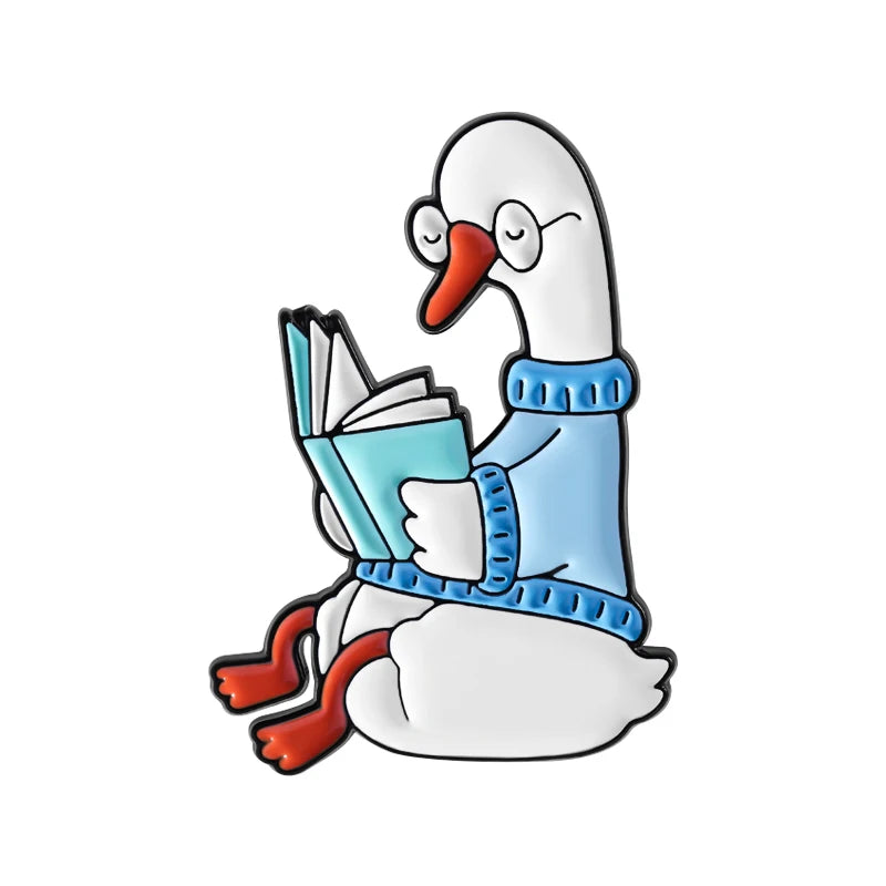 A white duck wearing a blue sweater is holding an open book, designed as an enamel pin.