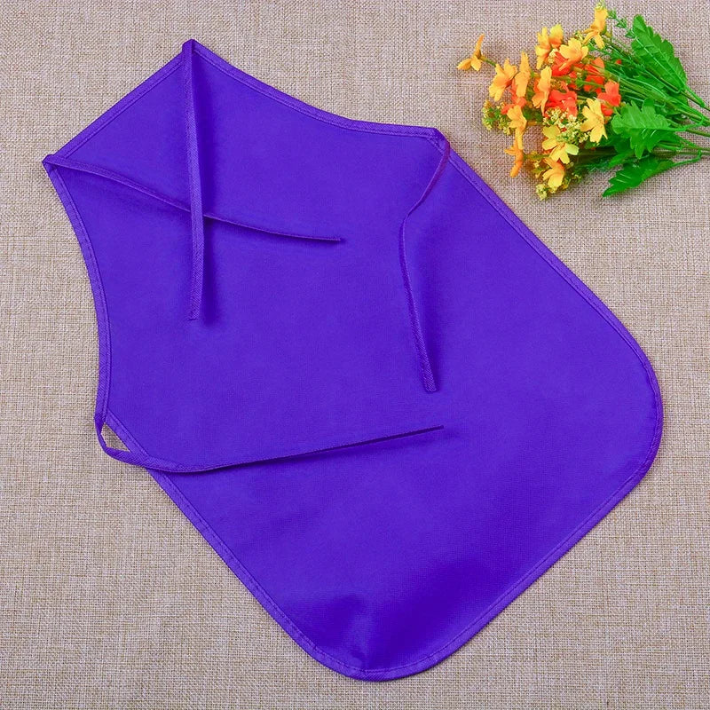 Purple non-woven fabric craft apron laid flat on a beige surface with a sprig of yellow flowers.