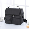A black insulated lunch bag with a handle and zippered compartments is shown on a white surface.