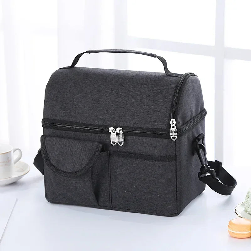 A black insulated lunch bag with a handle and zippered compartments is shown on a white surface.