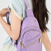 A purple quilted crossbody sling bag with a pink strap is worn by a person in a light blue top.