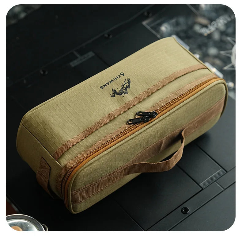 A beige portable storage bag for camping tableware with a brown zipper and strap, resting on a dark surface.