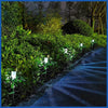 A row of garden lanterns illuminates a pathway through lush green foliage at night.