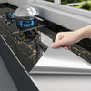 A hand is placing a silver cooking dome onto a black marble countertop, demonstrating a self-adhesive wall sticker product.