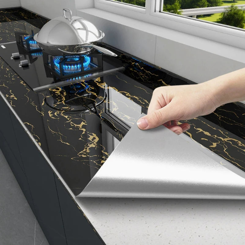 A hand is placing a silver cooking dome onto a black marble countertop, demonstrating a self-adhesive wall sticker product.
