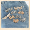 Silver and gold butterfly and crescent moon jewelry displayed on a denim fabric.