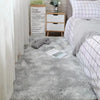 A fluffy gray silk-touch area rug placed in a bedroom setting next to a white cabinet and bedding.