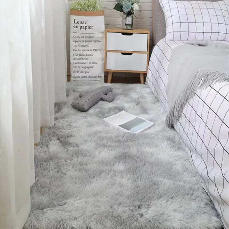 A fluffy gray silk-touch area rug placed in a bedroom setting next to a white cabinet and bedding.
