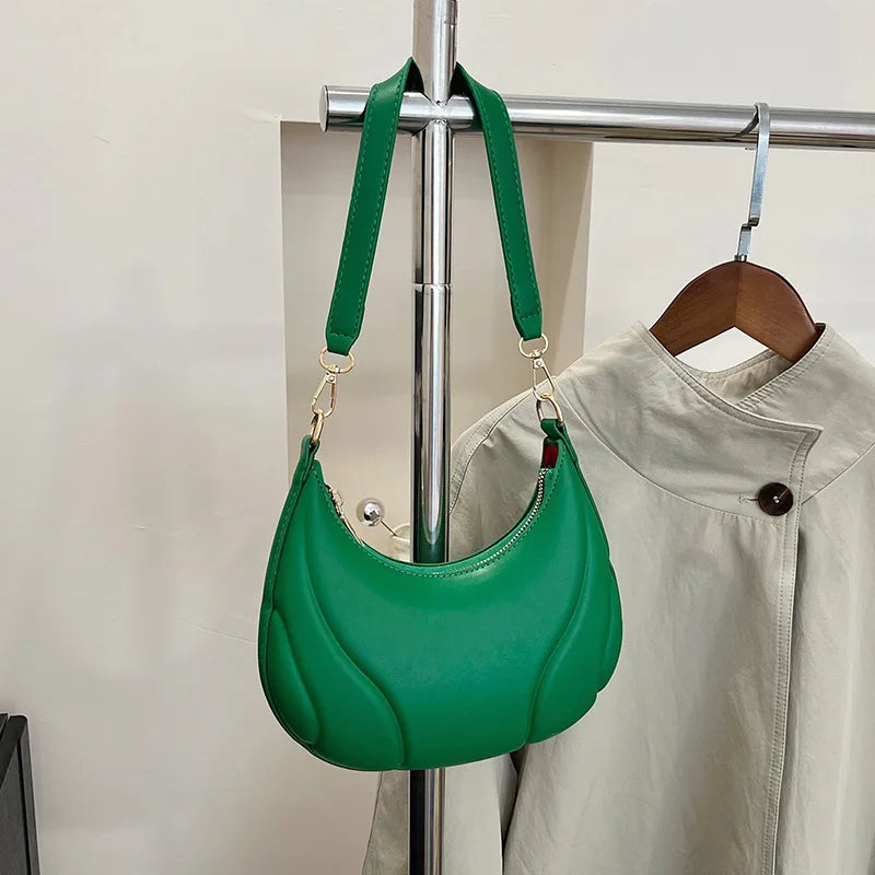 A green textured crossbody bag with a gold-tone adjustable strap is displayed on a hanger against a light background.