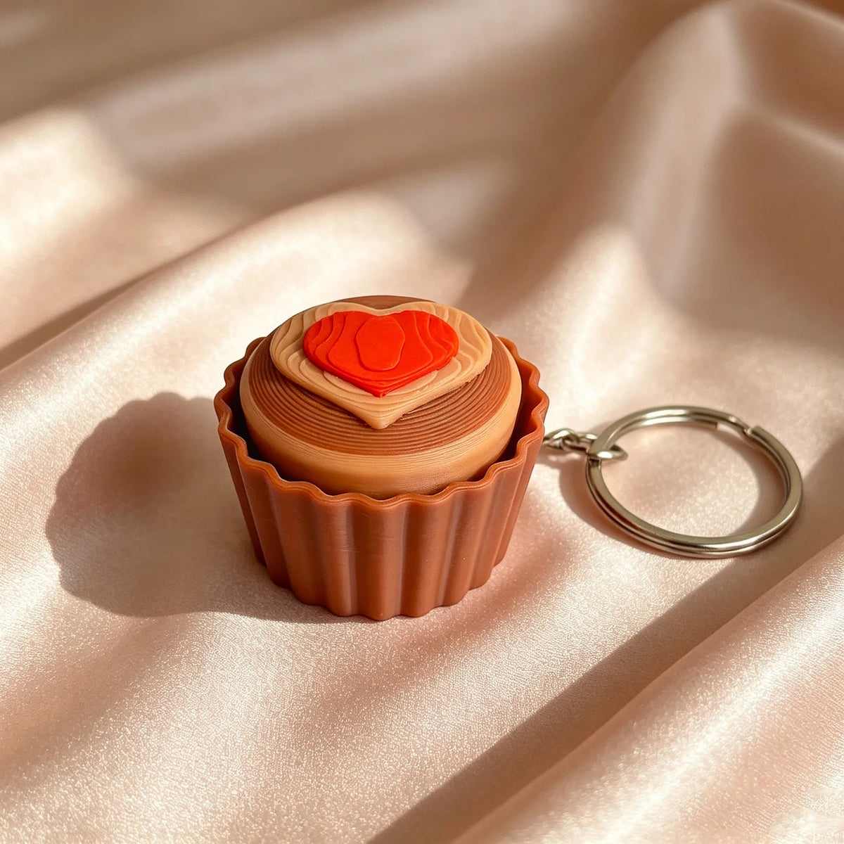 A small, round cake-shaped fidget keychain with an orange heart design set against a soft pink fabric background.