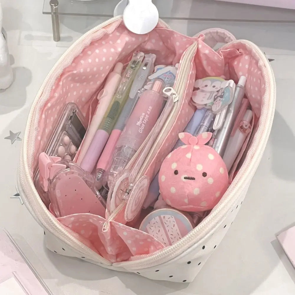 A pink polka dot shell-shaped pencil case with multi-compartment storage filled with pens and accessories.