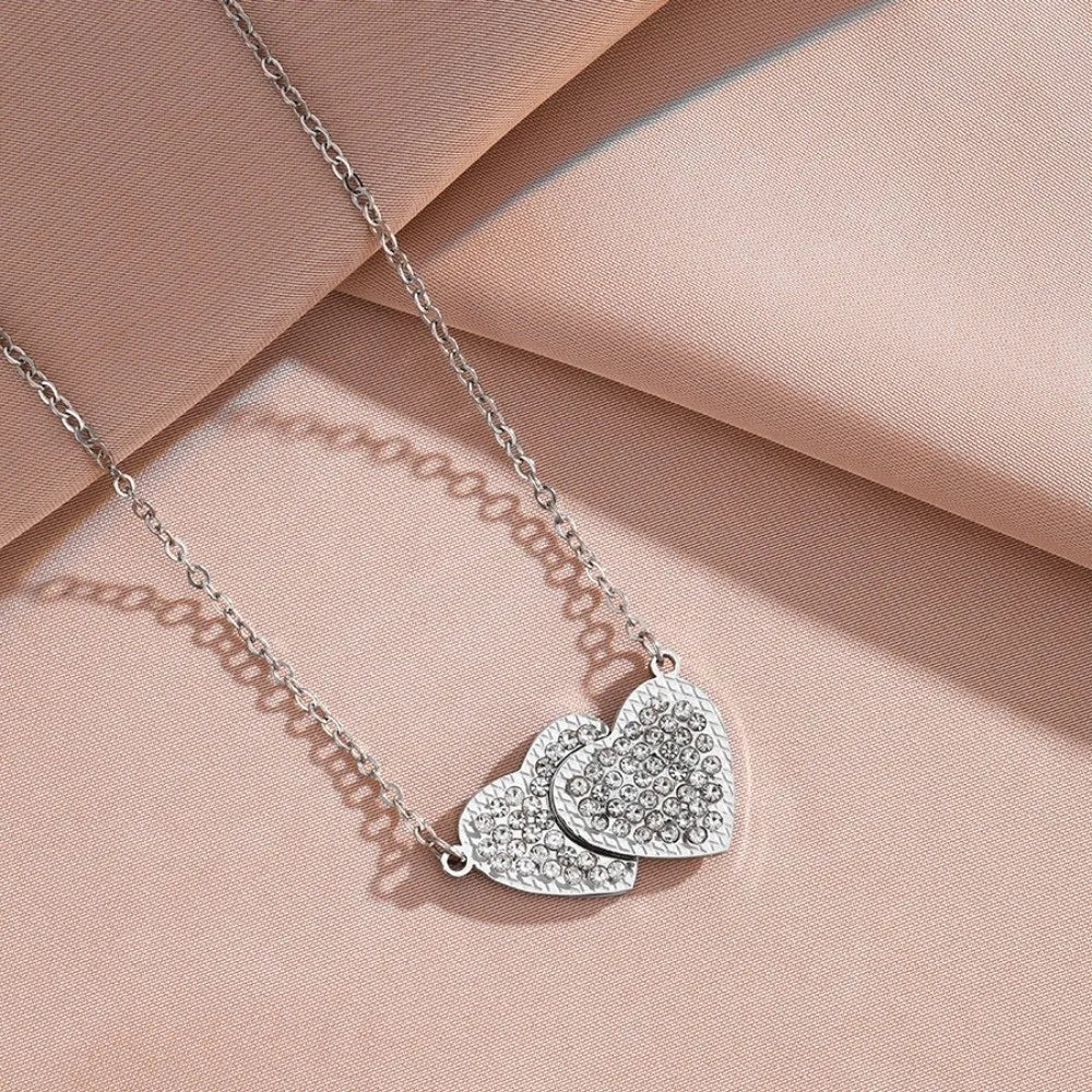 Silver heart pendant necklace with a textured chain resting on a pink fabric background.