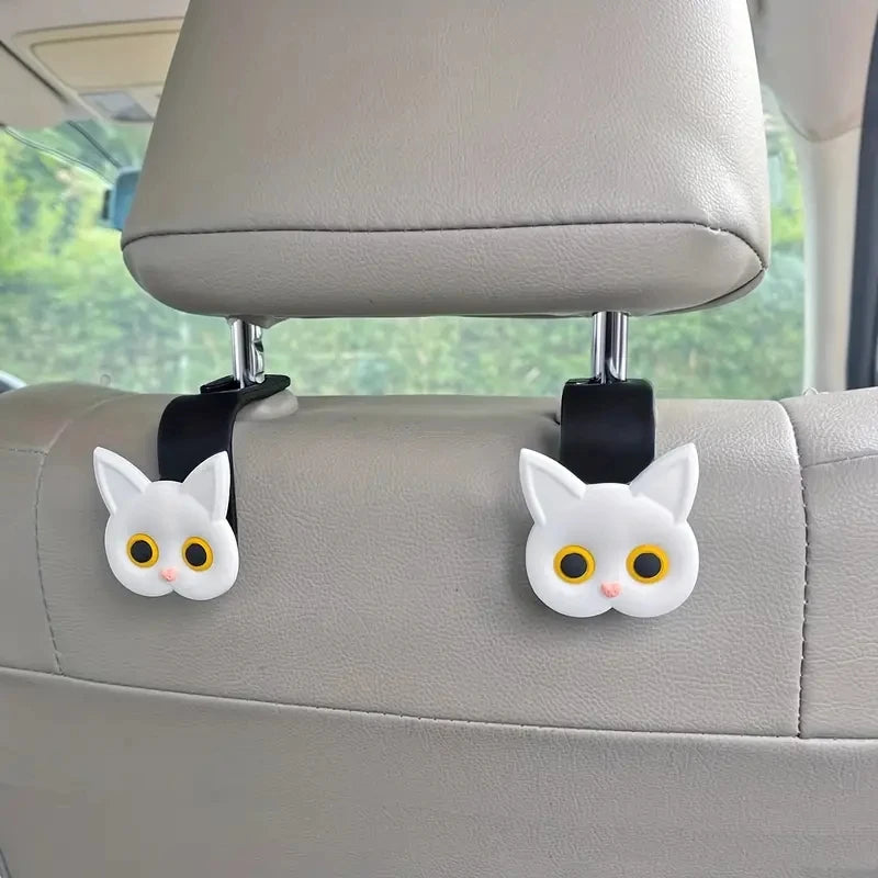 A set of two adorable white cat-shaped headrest hooks attached to a car seat.