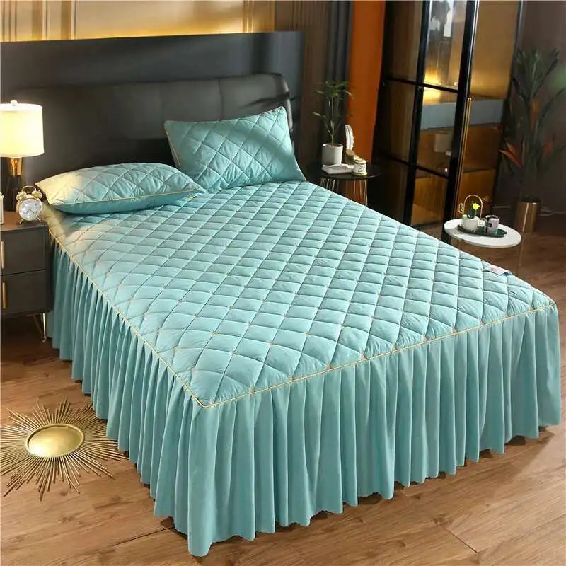 A teal quilted bed skirt with a diamond pattern and a matching pillow is displayed on a bed.