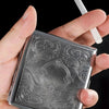 A hand holds a classic stainless steel cigarette case with an embossed floral pattern.