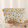 A hand holds a floral patterned corduroy makeup bag with a secure zipper against a white background.