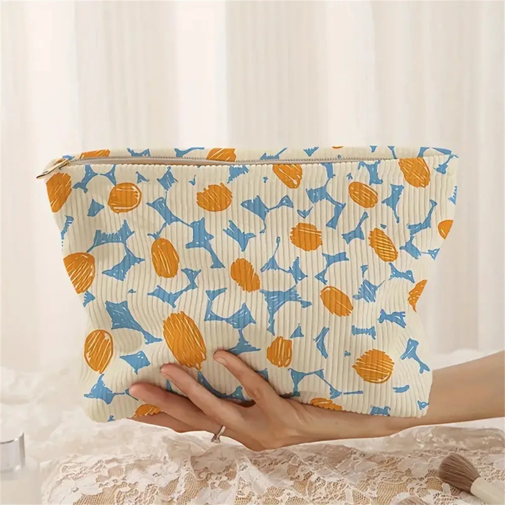 A hand holds a floral patterned corduroy makeup bag with a secure zipper against a white background.