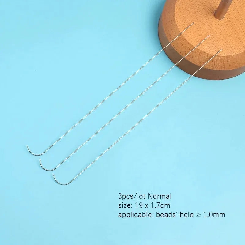 Three curved stainless steel beading needles laid diagonally on a light blue surface.