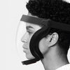 A close-up of a person wearing a black full face anti-fog shield with a clear lens and adjustable strap.