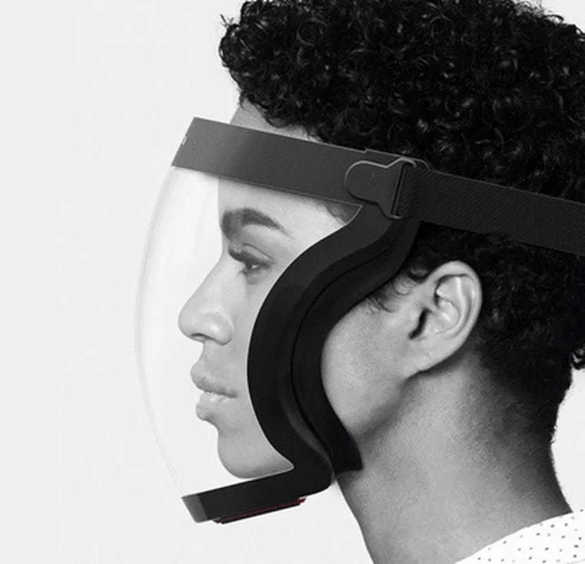A close-up of a person wearing a black full face anti-fog shield with a clear lens and adjustable strap.