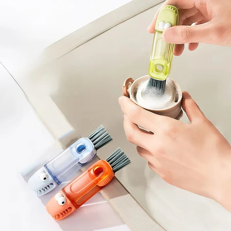 A hand is using a yellow cleaning brush to clean a glass bottle, with other brushes visible nearby.